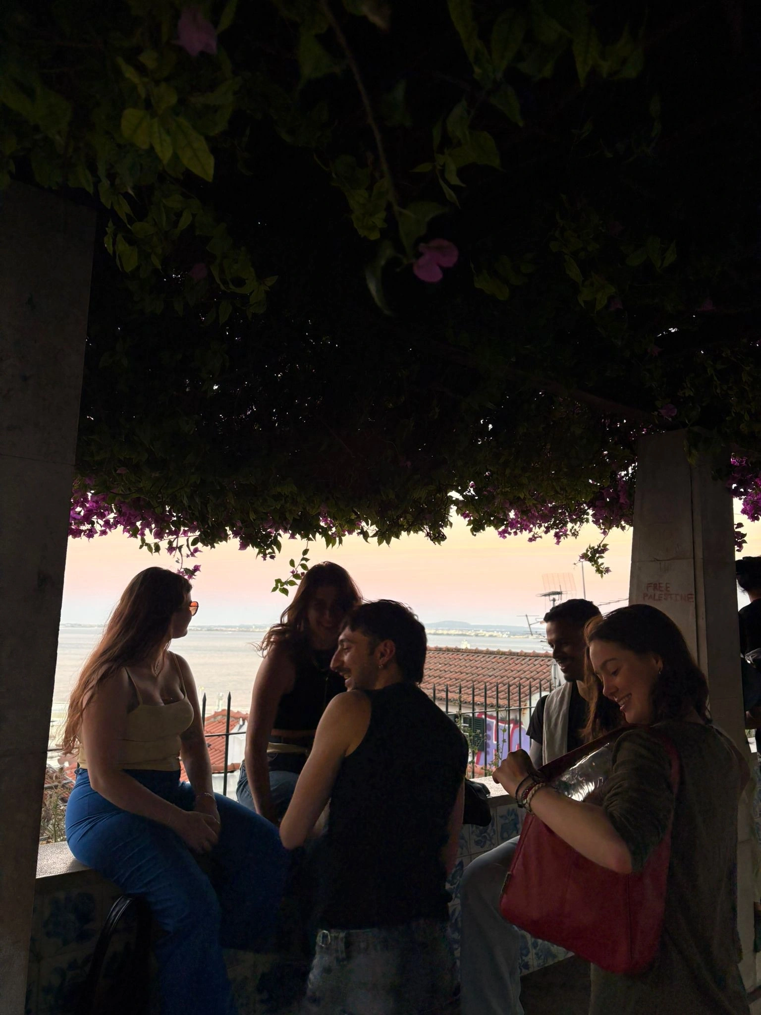 Friends chatting beneath a tree at a Lisbon viewpoint